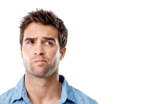 A man with a thoughtful expression looks slightly puzzled, wearing a blue button-up shirt.