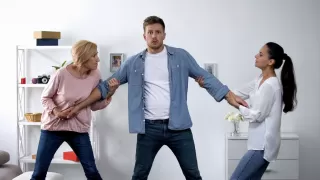 Two women pull a man in different directions, showing tension in a domestic setting.
