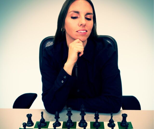 A woman thoughtfully considers her next move in a chess game, with black pieces on the board.