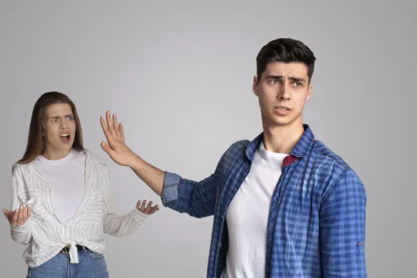 A frustrated young woman gestures while a man raises his hand, blocking her. Tension is evident between them.