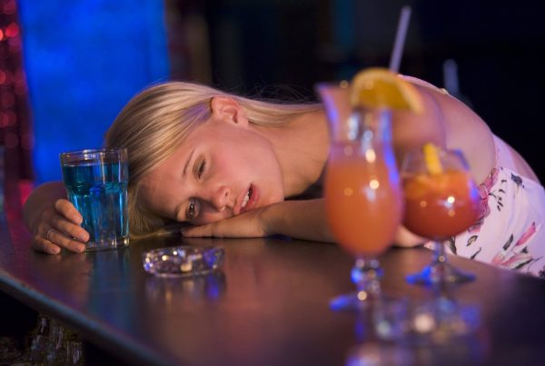 Woman resting her head on a table beside several drinks.